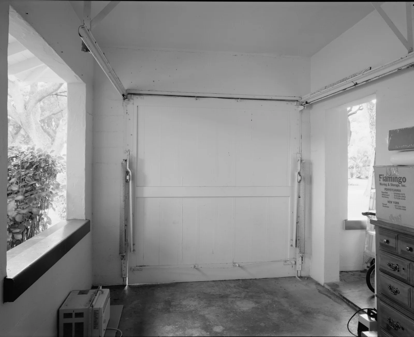 An empty garage seen from inside, facing a closed overhead door beside a window