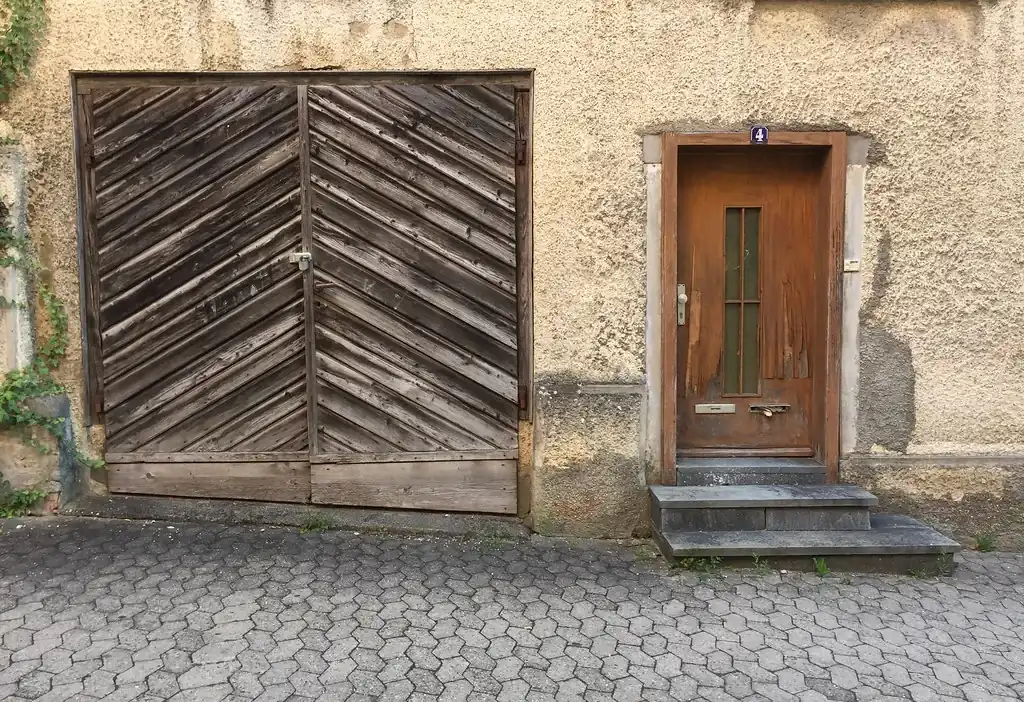 A weathered wooden garage door beside a small house door in a stucco wall